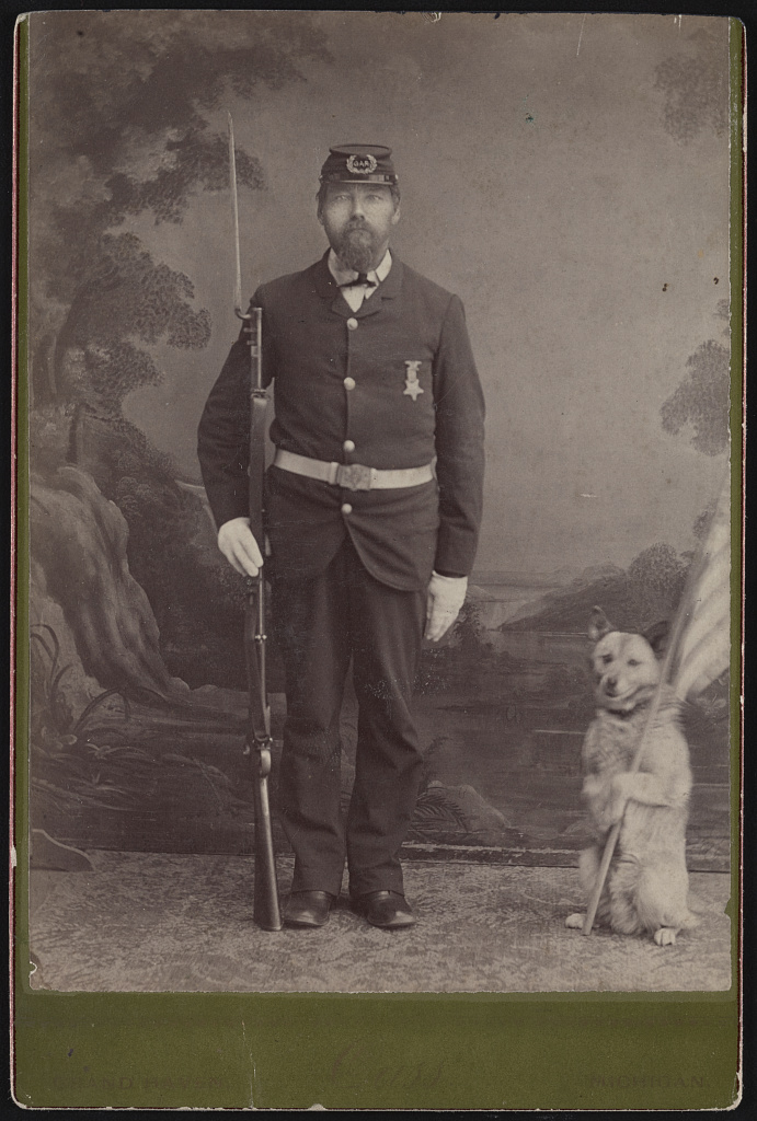 [Civil War veteran holding bayoneted rifle and dog holding flag in front of painted backdrop], 1870 (Library of Congress)