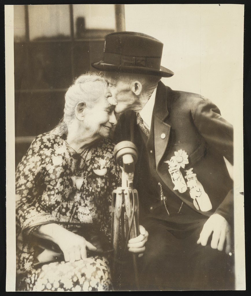 [Civil War veteran Private William Washington Nixon of Co. I, 2nd Pennsylvania Heavy Artillery Regiment wearing badges giving nurse Alice Cary Risley a kiss on her forehead at G.A.R. reunion in Washin, 1936 (Library of Congress)